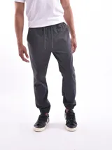 Pantalón tipo jogger color gris oscuro o negro, con cintura elástica y cordón ajustable, puños elásticos en los tobillos y bolsillos laterales.