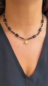 Collar corto tipo gargantilla compuesto por cuentas negras facetadas y cuentas negras ovaladas, separadas por pequeñas cuentas doradas. Incluye un dije colgante con forma de estrella de ocho puntas dorada.