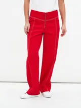 Pantalón de corte recto y tiro alto, color rojo, con costuras decorativas en contraste y cierre frontal con cremallera expuesta.