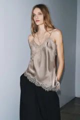Top lencero negro de escote pico y tirantes finos. Presenta aplicación de encaje a tono en el escote y el bajo asimétrico.
