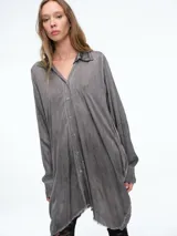 Camisa de corte oversize y silueta fluida, con cuello clásico, cierre frontal de botones y ruedo irregular con acabado desflecado.