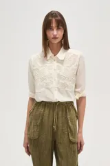 Camisa blanca de corte clásico con cuello camisero y cierre frontal de botones. Presenta un delicado diseño de encaje tipo crochet en la parte superior delantera, aportando un estilo romántico y artesanal.