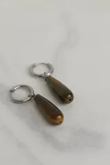 Aros tipo argolla de acero quirúrgico con dije colgante en forma de gota de piedra natural en tono marrón.
