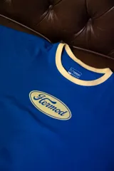 Remera oversize de algodón elastizado, color azul vibrante, con cuello redondo ribeteado en color beige claro. Presenta un estampado frontal ovalado en color beige claro con la palabra "Hermod" en tipografía cursiva.