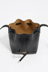 Bolso tipo saco de tamaño pequeño confeccionado en piel vacuna negra, con cierre de cordón ajustable, asa larga regulable y logo de la marca en letras metálicas doradas en la parte frontal.