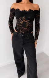 Body de encaje negro con diseño off-shoulder, mangas largas y escote con terminación en picos.