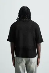Camiseta de punto negro, corte relajado, con cuello redondo amplio y manga corta. El tejido es ligero y calado.