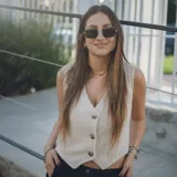 Chaleco corto con estampado abstracto en tonos dorados y azules, escote en V y cierre frontal con botones de madera.