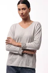 Buzo de manga larga con escote en V, confeccionado en tejido suave y liviano con calce relajado. Presenta un diseño liso en color gris con puños que, al doblarse, revelan un estampado animal print.