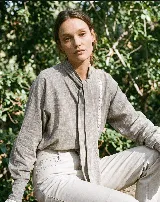 Camisa gris de algodón con textura sutil, corte relajado y mangas amplias. Cuenta con cuello mao con lazo largo para anudar, y detalles de puntilla blanca a contratono en la parte delantera y en los puños.