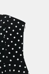 Top de escote recto y hombros descubiertos, color negro con estampado de lunares blancos. Presenta diseño entallado con bajo acabado en peplum y cierre lateral con cremallera oculta.