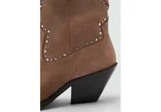 Botines de estilo texano en color marrón claro, confeccionados en piel bovina, con diseño de caña baja, puntera fina y detalles de tachas metálicas en la parte frontal y lateral.