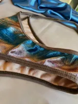 Conjunto de bikini confeccionado en terciopelo con efecto degradado en tonos azul, marrón y rosado. El corpiño es de estilo triangular con aros metálicos decorativos en el centro y breteles regulables. La bombacha es de corte clásico con laterales ajustables mediante tiras.