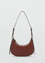 Cartera de hombro tipo hobo en color marrón, confeccionada en material efecto piel. Presenta un diseño de media luna con costuras visibles en contraste, cierre superior de cremallera y asa ajustable mediante hebillas metálicas.