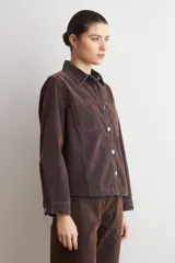 Sobrecamisa de jean con acabado simil terciopelo en color marrón oscuro, de corte recto, manga larga, cuello clásico y cierre frontal con botones metálicos.