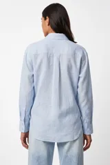 Camisa de manga larga color celeste, con cuello clásico, cierre frontal con botones y un bolsillo aplicado en el pecho.
