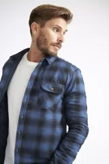 Sobrecamisa de viyela para hombre con estampado de cuadros en rojo y negro. Presenta cierre frontal con botones, bolsillos en el pecho con solapa y botón, y un interior capitoneado para mayor abrigo. Cuenta con un logo en grifa de cuero.