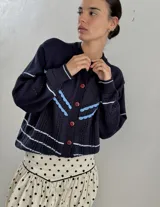 Saco de punto color crema con detalles en crochet verde, cierre frontal con botones y mangas largas.