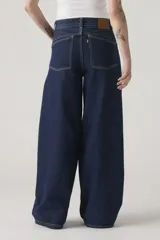 Jean de corte baggy y silueta barrel, confeccionado en denim rígido de color azul oscuro. Presenta costuras laterales curvadas que definen su forma característica, tiro alto y cierre frontal con botón y cremallera.