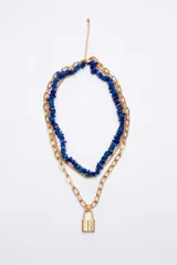 Collar triple dorado compuesto por una cadena de eslabones gruesos con dije de candado, una cadena fina y una gargantilla de piedras naturales azules en forma de viruta.