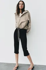 Campera estilo cazadora con capucha ajustable con cordones, cierre frontal de cremallera, mangas largas con puños elásticos, bolsillos delanteros de doble vivo y bajo ajustable con cordones. Presenta un diseño de cuadros en tonos beige y marrón.