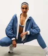 Campera deportiva tipo parka confeccionada en microfibra azul, con cuello alto, cierre frontal por cremallera, mangas largas con puños elásticos y detalle de fruncido lateral ajustable.