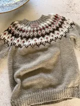 Sweater tejido a mano de corte clásico, color gris con diseño de guarda nórdica en el canesú en tonos blanco, marrón y detalles en rojo.