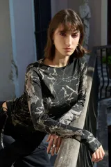 Top de manga larga color negro, confeccionado en jersey elástico. Presenta un diseño asimétrico con jaretas laterales regulables que permiten ajustar el largo y el volumen, y aberturas para los pulgares en los puños.