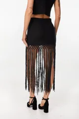 Falda corta negra de tejido de punto con detalle de crochet en la parte inferior y largas tiras colgantes a modo de flecos.