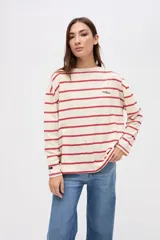 Remera de manga larga con diseño a rayas horizontales en color crema y rojo. Presenta un corte holgado, cuello redondo y un pequeño bordado en el pecho.