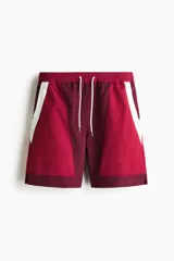 Short deportivo de nylon en bloques de color rojo, bordó y blanco. Cuenta con elástico revestido y cordón de ajuste blanco en la cintura, bolsillos laterales, aberturas cortas en el bajo y suspensor interior de malla.