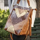 Bolso marrón de cuero vacuno con apliques de cuero con textura de cocodrilo y detalles dorados. Tiene manija corta y correa ajustable y removible para usar como morral. Cuenta con dos bolsillos verticales en el fuelle, uno de cada lado. El interior está forrado y tiene un bolsillo con cierre y otro pequeño para el móvil.