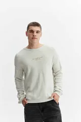 Sweater oversize de tejido liviano color gris claro, con hombros caídos, cuello redondo, costuras a la vista y bordado sutil en el pecho.