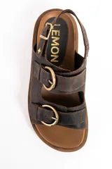 Sandalias de cuero marrón oscuro, con doble tira ancha en el empeine y tira en el talón, todas con hebillas metálicas doradas. Cuenta con suela plana y gruesa de tono tostado con estriado inferior.