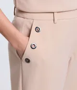 Pantalón slim color beige, confeccionado en crepé, con cierre delantero en la cintura y detalles de ojales en los bolsillos.