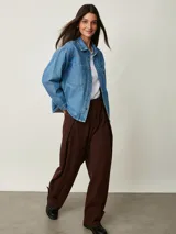 Camisa de denim celeste oversize con bolsillos frontales, cierre de botones metálicos y detalles de tachas en el cuello y la parte delantera.
