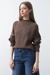 Polera de punto color marrón, con cuello alto y diseño de trenzas verticales en el frente y tejido acanalado en las mangas. Presenta mangas raglán y terminaciones acanaladas en puños y ruedo.