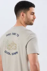 Remera de manga corta color gris claro, de corte clásico y cuello redondo. Cuenta con un diseño estampado en la espalda que incluye un paisaje de montaña con cactus y la frase "Take time to cool down".