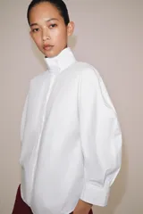 Camisa blanca de algodón de la colección ZW Collection de Zara, con cuello alto, mangas abullonadas por debajo del codo y cierre frontal con botones ocultos por solapa.