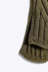 Top de tejido de punto acanalado color verde militar, con cuello alto tipo tortuga y mangas sisa. Presenta un bajo asimétrico con aberturas laterales.