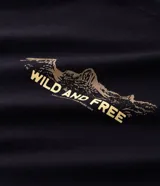 Remera negra de corte comfort, con cuello redondo, manga corta y estampa lettering en el pecho con diseño de montañas y el texto "WILD AND FREE".
