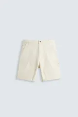 Bermuda de algodón color crema, corte relajado (relaxed fit), con cinco bolsillos y detalles de bolsillo multifunción en la pernera, estilo carpintero. Presenta efecto lavado y terminación de ruedo deshilachada.