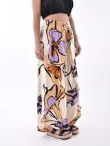 Pantalón palazzo estampado con flores en tonos violeta, naranja y beige sobre fondo crema, con cintura elástica y cordón ajustable.