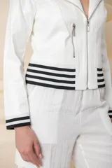 Chaqueta azul de cuero ecológico con cierre frontal asimétrico y cuello con solapas. Tiene puños elásticos a rayas blancas y azules, cierres metálicos plateados y un bolsillo en la manga.