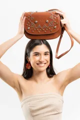 Bandolera de cuero negro con estructura rígida, tapa frontal decorada con tachas metálicas plateadas colocadas a mano y correa larga ajustable.