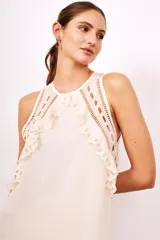 Vestido sin mangas color crema, con cuello redondo y detalles de volados y bordados calados en el frente. El tejido principal presenta pequeños puntos en relieve.