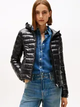 Campera puffer ultraliviana de color negro con acabado brillante, diseño acolchado horizontal y capucha. Presenta cierre frontal de cremallera, bolsillos laterales con cierre y logo engomado de Tommy Hilfiger en la manga. Confeccionada en nailon reciclado con corte regular.