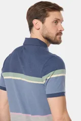 Remera polo de manga corta con diseño de franjas horizontales en tonos azul, gris, verde y detalles en rosado. Cuenta con cuello clásico y cierre frontal de botones.