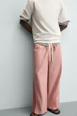 Pantalón de corte relajado confeccionado en popelín de algodón, con estampado de rayas verticales blancas sobre fondo rosado. Posee cintura elástica ajustable con cordón y bandas laterales lisas en color rosado oscuro, ribeteadas con un vivo blanco.