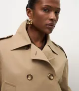 Trench coat corto de la marca Cortelle, confeccionado en una mezcla de algodón y poliéster. Presenta un diseño estructurado con cierre cruzado de botones, cuello clásico, mangas largas con trabillas en los puños y bolsillos frontales.